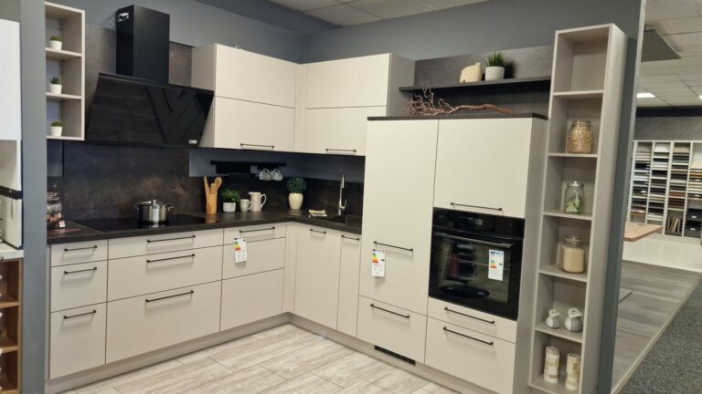Bauformat-Küche über Eck in der Ausstellung des Küchen Profi Center Dresden: cremefarbene Fronten mit schwarzen Griffen, dunkle Arbeitsplatte, Backofen in Griffhöhe